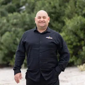 Man posing for headshot on sand with trees behind him