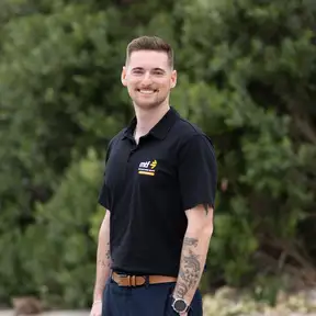 Man standing on sand posing for a headshot with trees behind him
