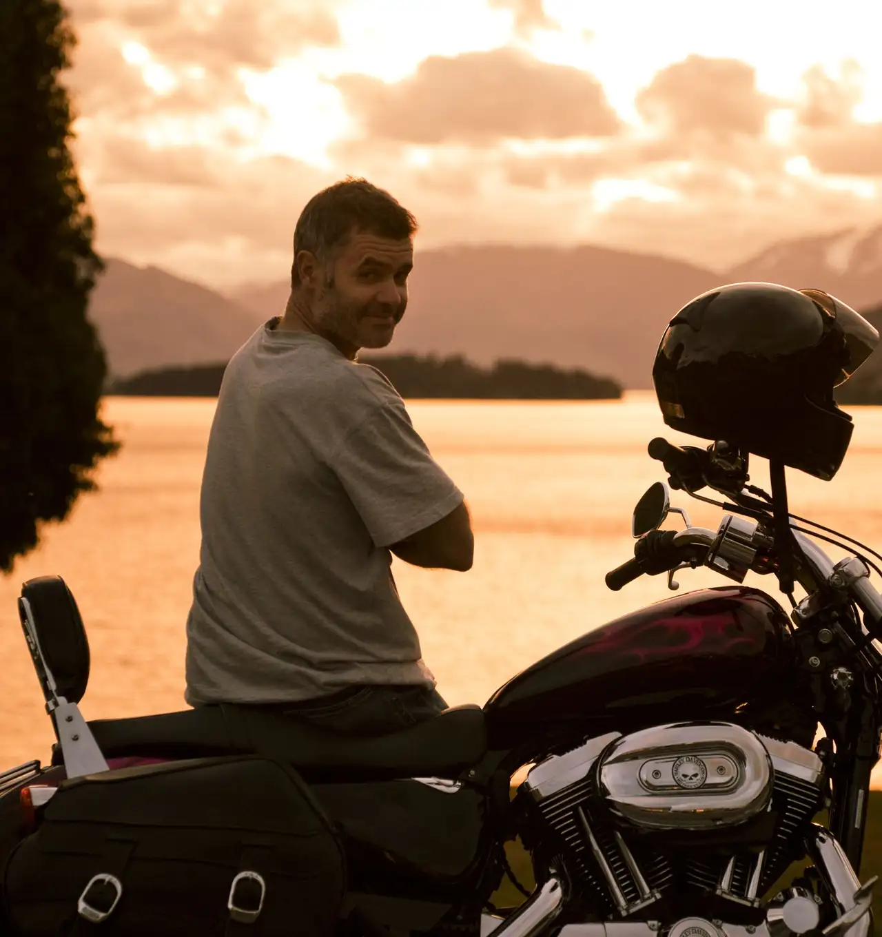 A man leaning against a motorcycle at sunset