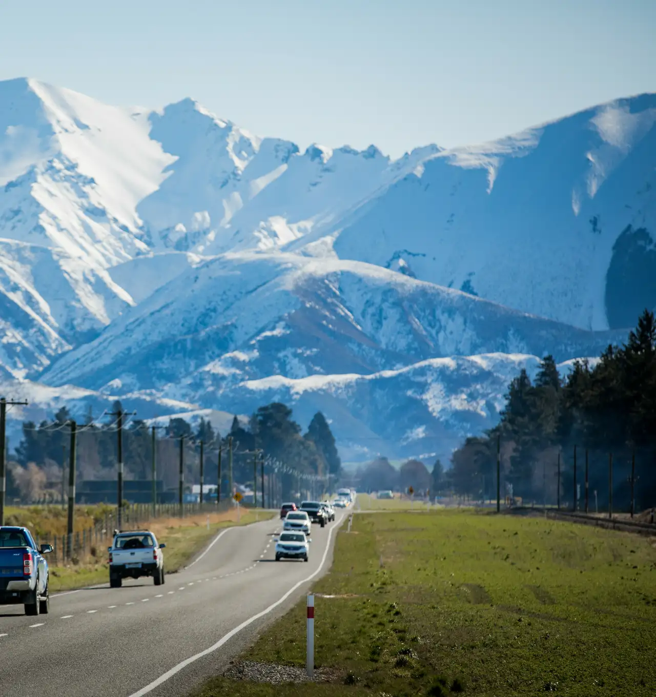 Cars driving along a road with snow covered mountains in the background