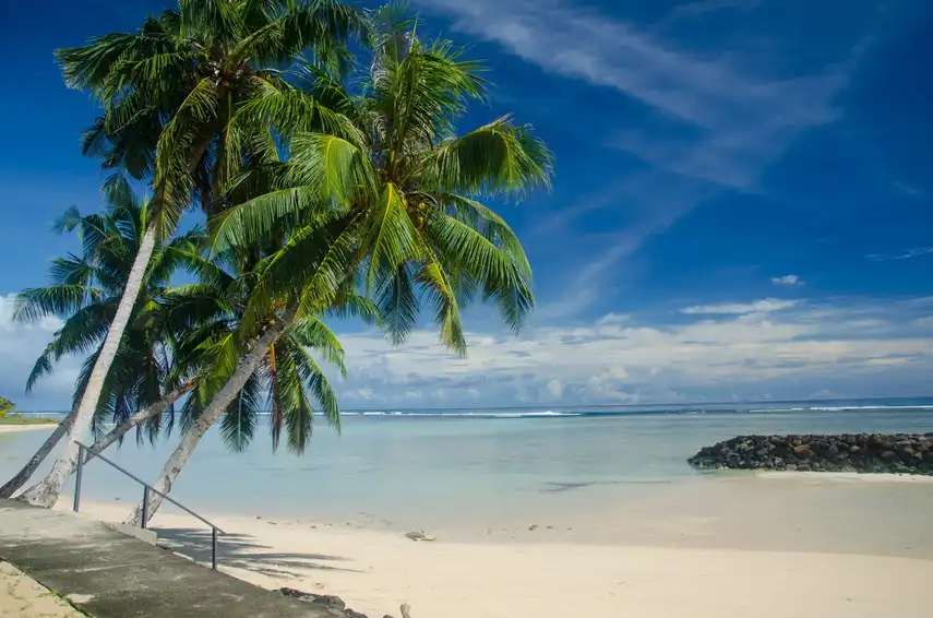 A beach surrounded by palm trees, blue sea and a cloudy sky in Manase, Samoa